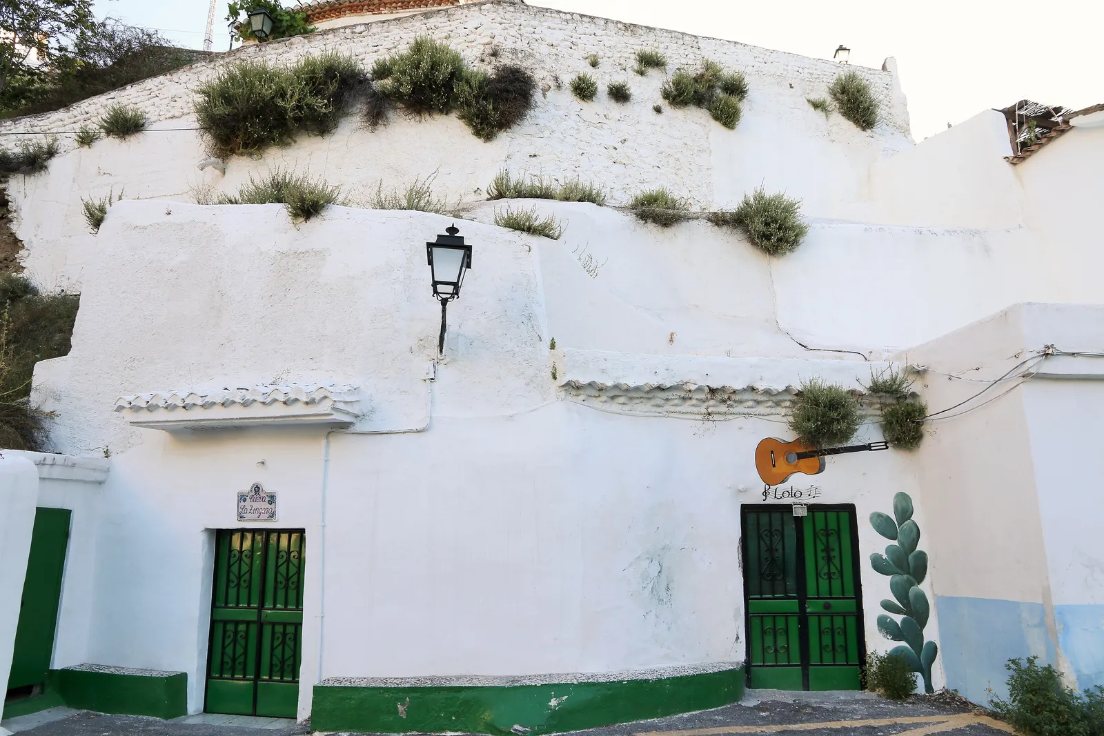 Ein weiß getünchtes Höhlenhaus in Sacromonte mit zwei grünen Türen, einer Laterne und einer an der Wand befestigten Gitarre; eine allgemeine Aufnahme des Viertels, nicht die Höhle dieses Tickets